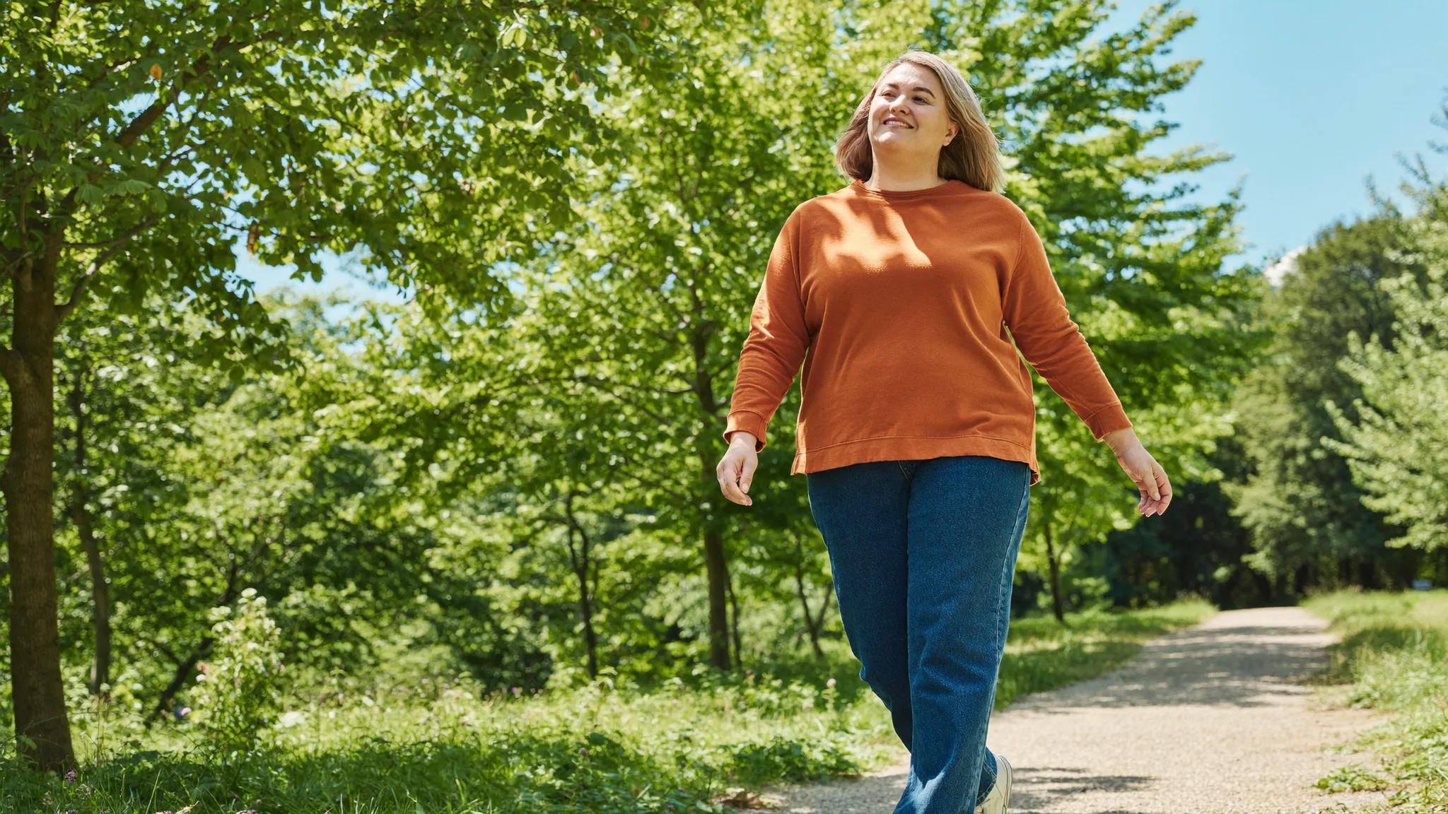 A woman striding through a sunlit park path