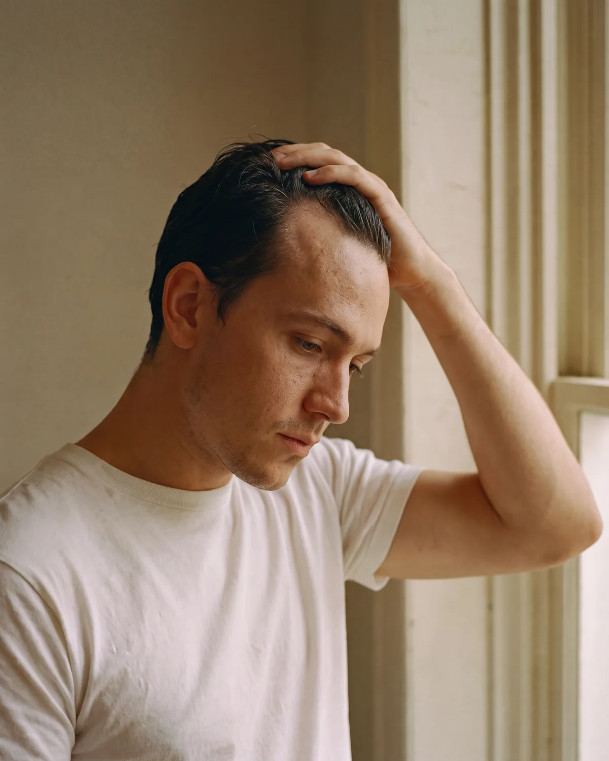 A man by a window running a hand back through his hair