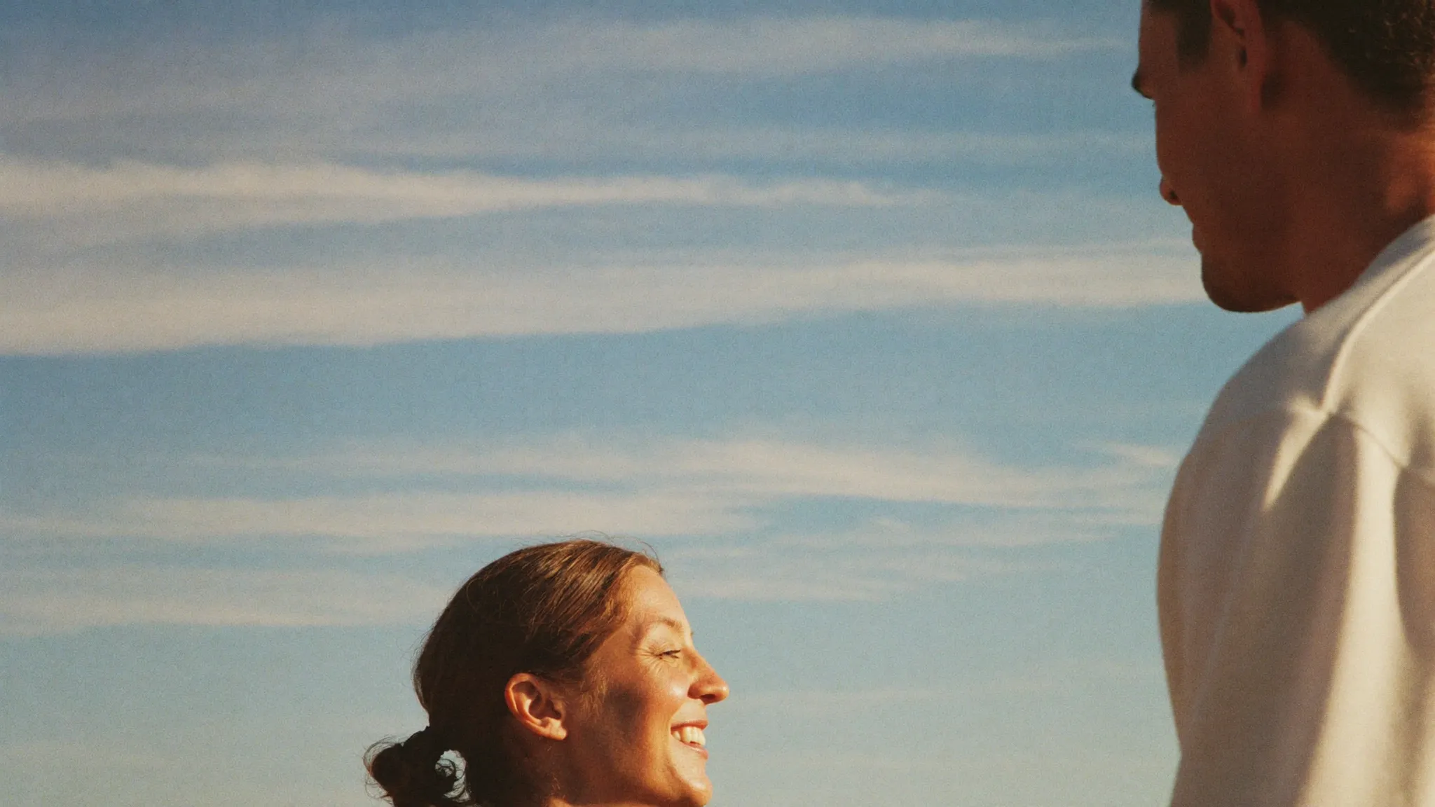 A couple outdoors under a wide blue sky, smiling into the light