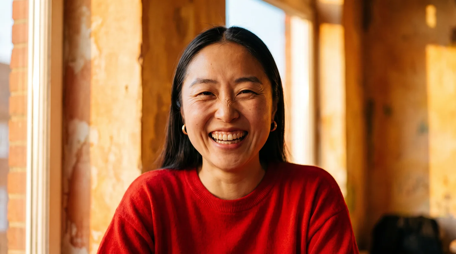 A woman in a red jumper laughing by a bright window