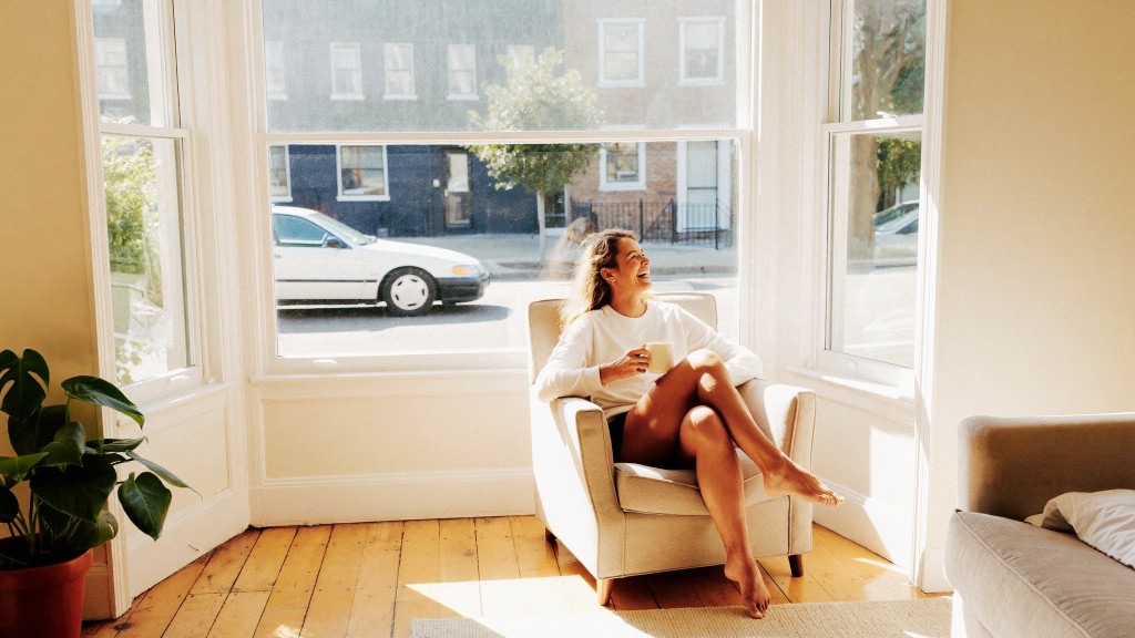 A woman laughing in a sunlit armchair by a bay window, mug in hand